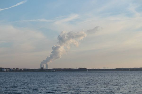 Braunkohlekraftwerk am Horizont, davor Wasser, Abgase steigen aus Schornsteinen