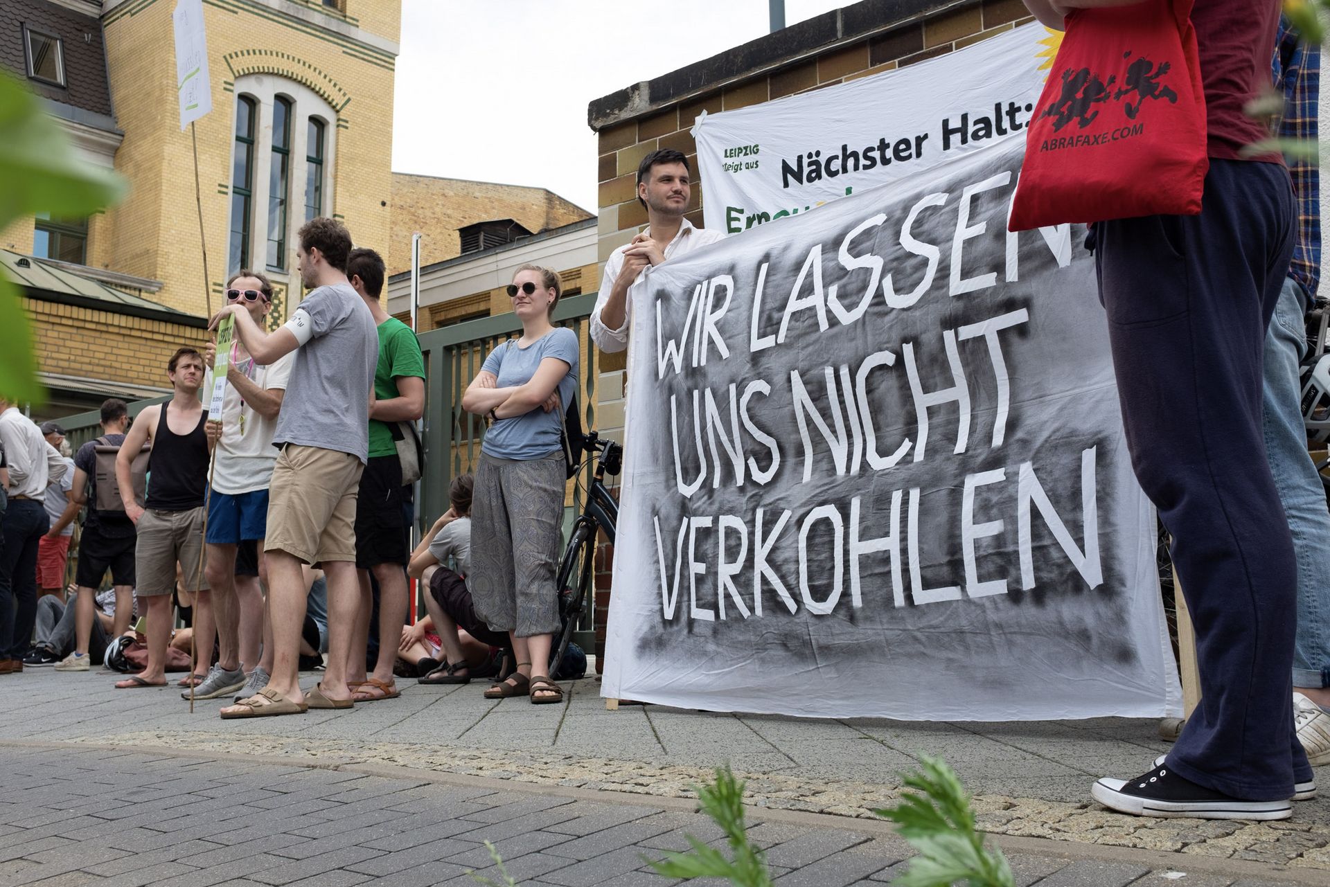 Menschen demonstrieren vor Stadtwerken, zwei halten ein Banner auf dem steht: "Wir lassen uns nicht verkohlen"