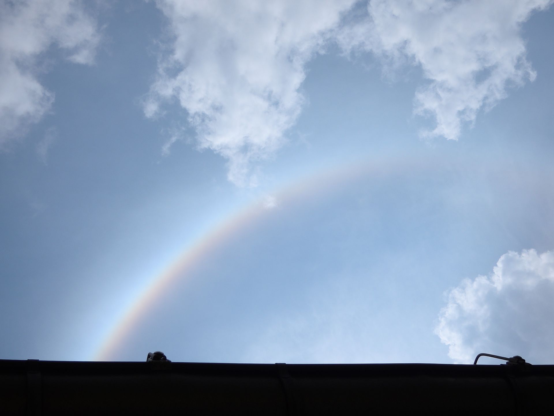 Regenbogen am Himmel mit Wolken über einem Dach