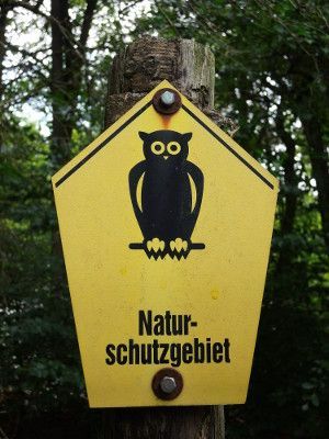 Schild eines Naturschutzgebietes, gelb mit Eule
