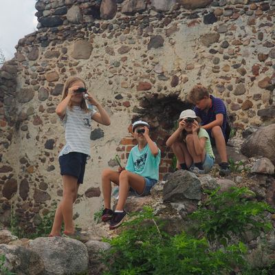 Kinder sitzen auf einer Ruine und schauen durch Ferngläser