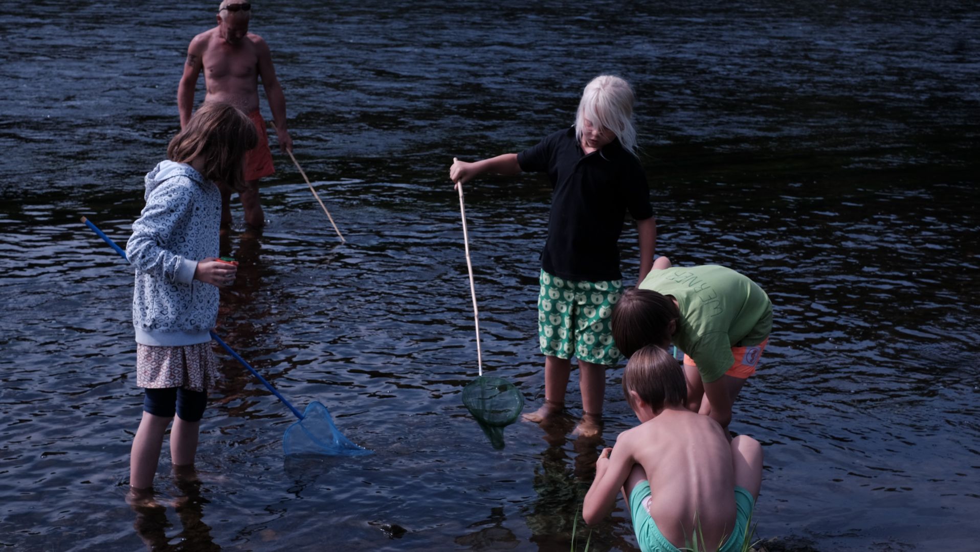 Kinder stehen im Wasser mit Keschern und Lupengläsern in der Hand und untersuchen das Wasser