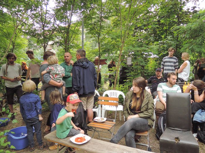 Menschen stehen im Schatten von Bäumen im Gemeinschaftsgarten VAGaBUND und unterhalten sich