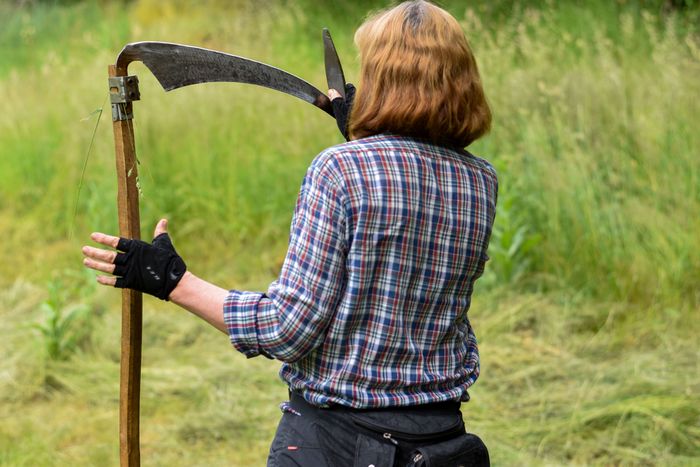 Frau von hinten zu sehen mit Sense in der Hand