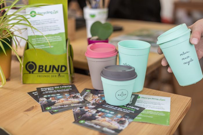 Recycling2go-Becher und Werbematerialien auf einem Holztisch. Sieht  wunderschön aus!