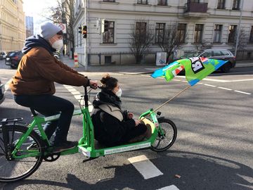 zwei Personen fahren mit einem Lastenrad und schwenken eine Fahne mit dem Aufdruck "Klima retten"