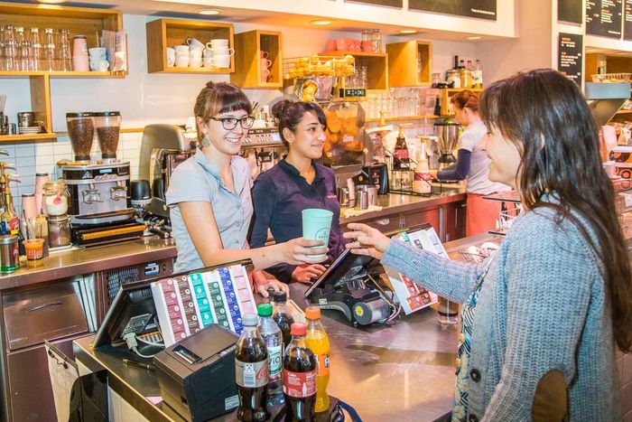 An der Kasse in einen großen Bäckerei-Gastronomie: Ein Recup-Pfandbecher wird übergeben.