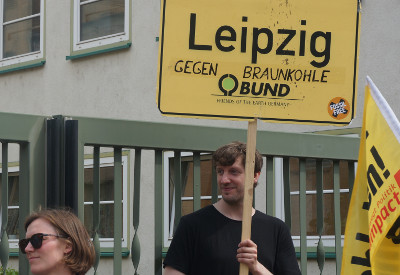 Mann hält Leipziger Ortsschild auf dem steht: "Leipzig gegen Braunkohle"; darunter BUND-Logo