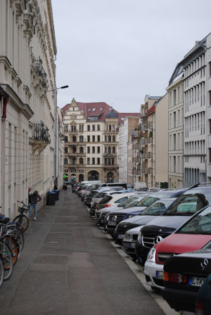 Fußweg neben Altbauten, viele parkende Autos